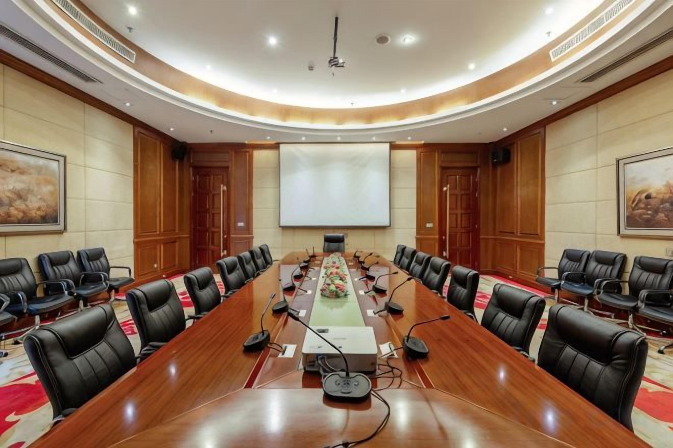 A conference room with a long table, multiple chairs, a projector screen, and a large painting on the wall.