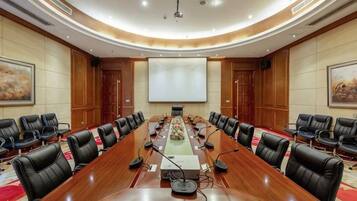 A conference room with a long table, multiple chairs, a projector screen, and a large painting on the wall.