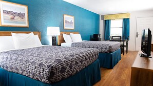 Quarto de hotel com duas camas, uma escrivaninha, uma cadeira, televisão e obras de arte nas paredes.