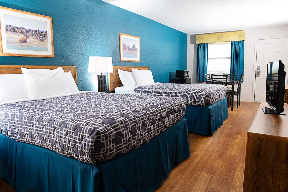 A hotel room with two beds, a desk, a chair, a TV, and artwork on the walls.