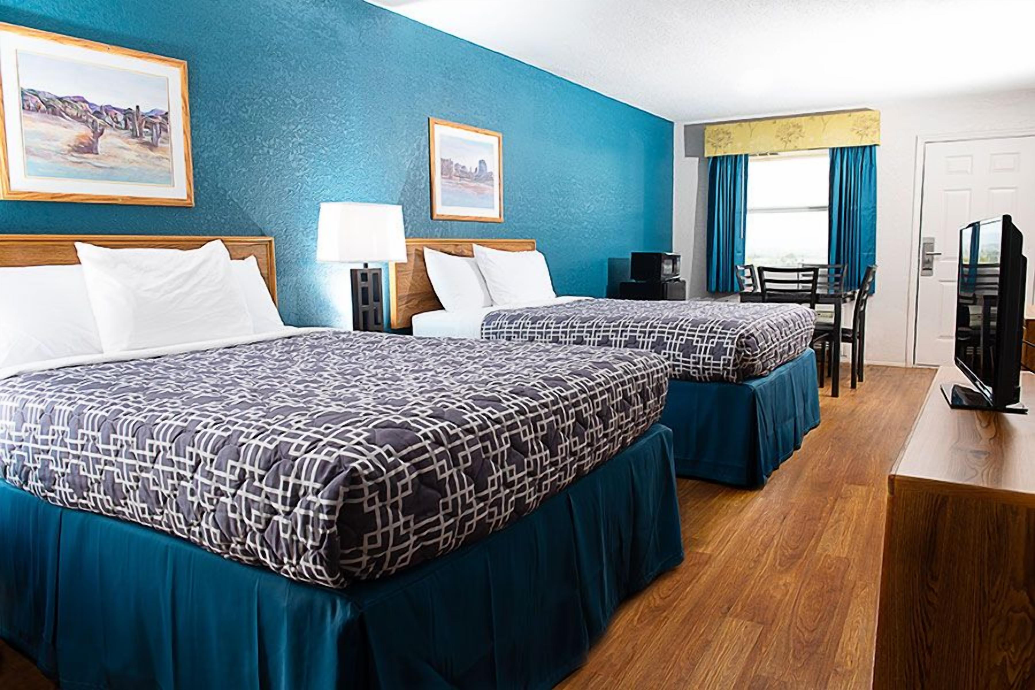 A hotel room with two beds, a desk, a chair, a television, and artwork on the walls.