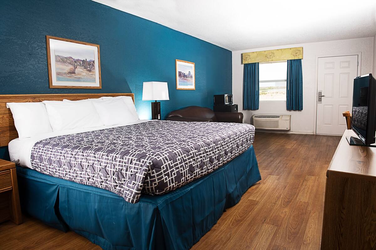 A hotel room with a large bed, a desk with a television, a desk lamp, and two framed pictures on the wall.
