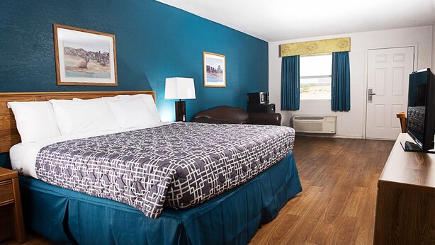 A hotel room with a large bed, a desk with a television, a desk lamp, and two framed pictures on the wall.
