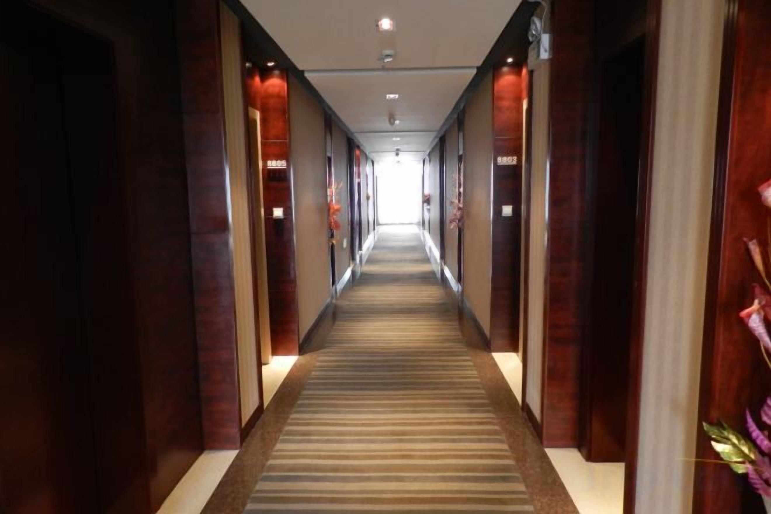 A hotel corridor with a carpeted floor, wooden paneling on the walls, and a light source at the end.