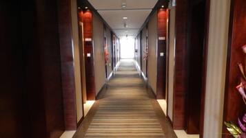 A hotel corridor with a carpeted floor, wooden paneling on the walls, and a light source at the end.