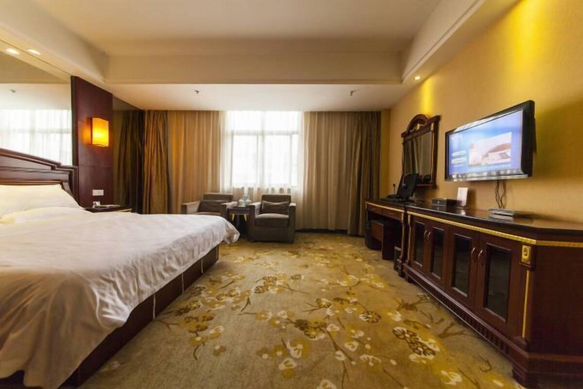 A hotel room with a large bed, a desk with a chair, a television, and a carpet with a floral pattern.