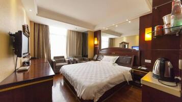 Habitación de hotel con una cama grande, un escritorio con computadora, una silla, un televisor y un mini bar.