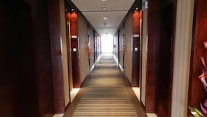 Un long couloir étroit, typique des hôtels, avec des lambris en bois sur les murs et un tapis à rayures.