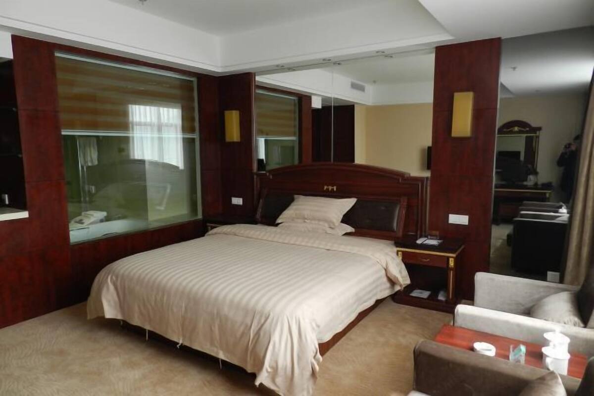A hotel room with a large bed, a wooden headboard, a bedside table, a chair, and a mirror.