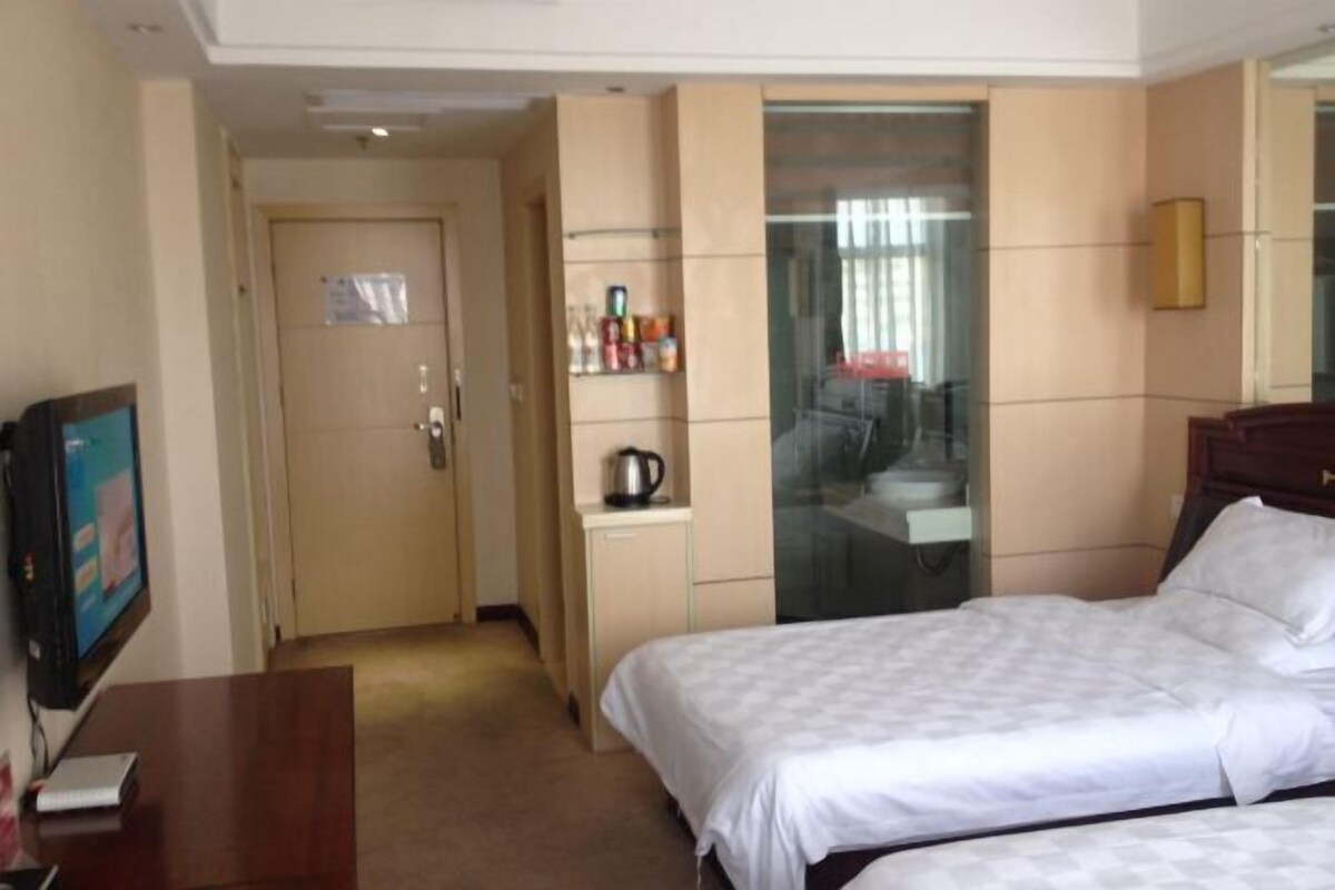 A hotel room with a bed, a desk, a TV, a minibar, and a glass-enclosed bathroom.