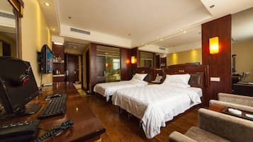 A hotel room with two beds, a desk with a computer, a chair, and a TV.