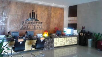 A hotel reception area with a marble wall, reception desk, computers, and seating.