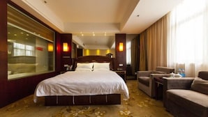Une chambre d’hôtel dotée d’un grand lit, d’un coin salon avec deux fauteuils, d’une cloison en verre et d’une grande fenêtre avec des rideaux.