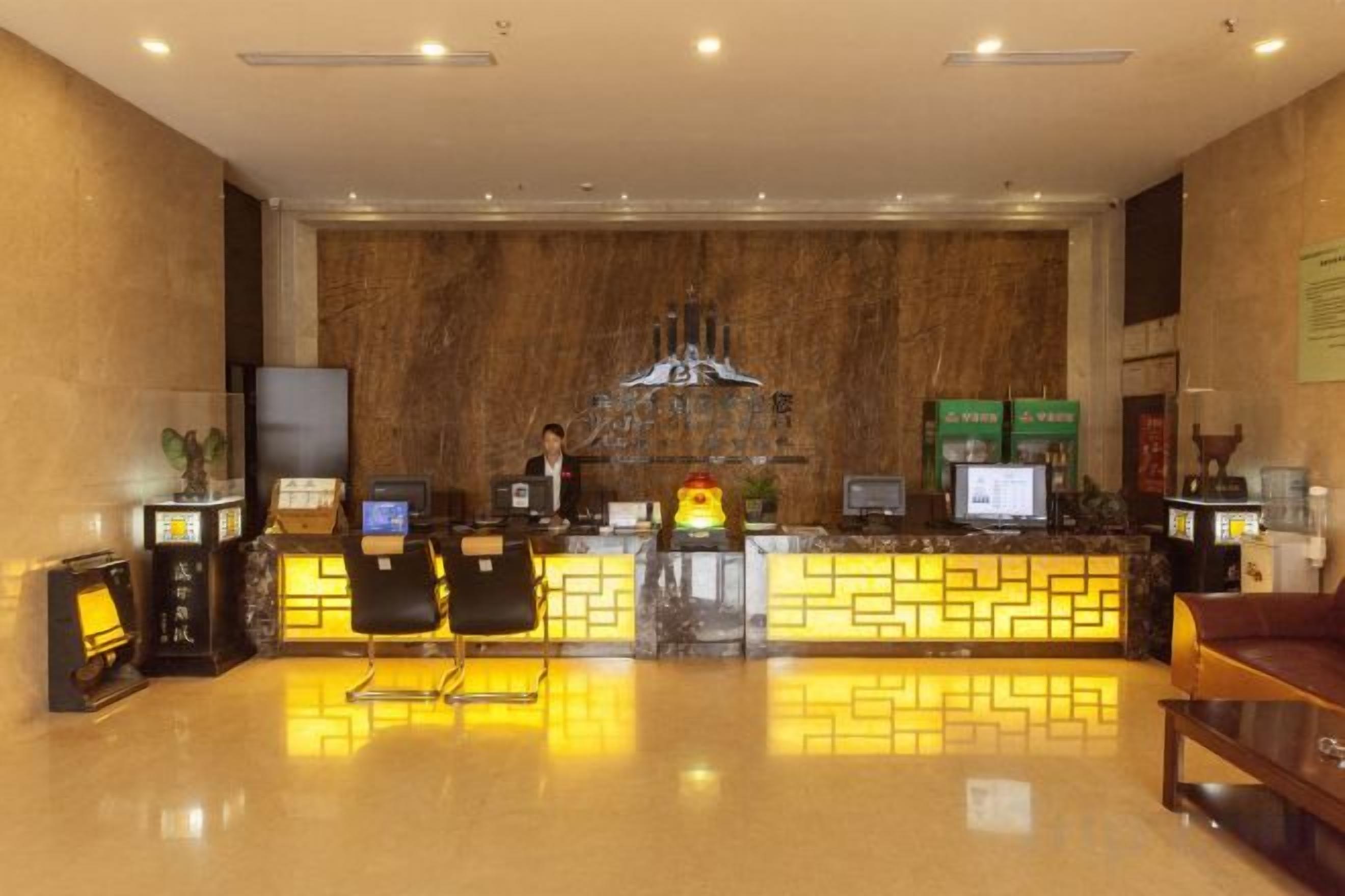 A hotel reception area with a marble wall, reception desk, two computer monitors, and a television.