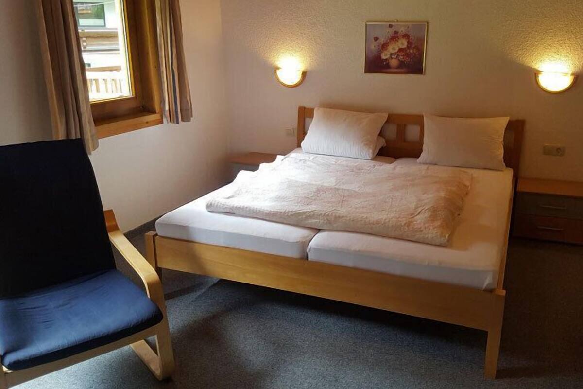 A single bed with a wooden frame and white bedding, a dark blue chair, and two bedside tables with lamps.