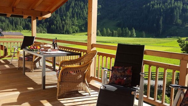 Un espacio al aire libre techado con una mesa lista para comer, sillas de mimbre y una parrilla.