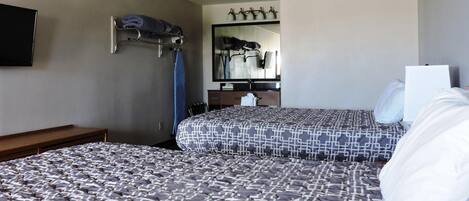 A hotel room with two beds, a mirror, a TV, and a coat rack.