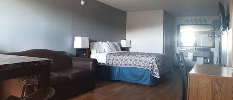 A compact hotel room with a bed, a small desk, a chair, a sofa, and a wooden cabinet.