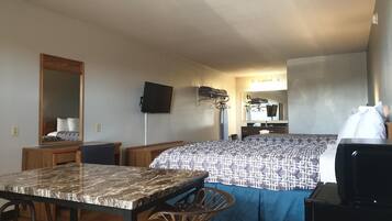A compact hotel room with a bed, a desk, a chair, a TV, and a mirror.