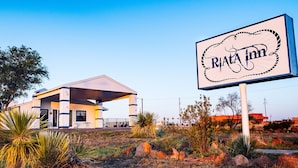 A modern building with a covered patio area, a sign for 'Rita Inn', and surrounding desert vegetation.