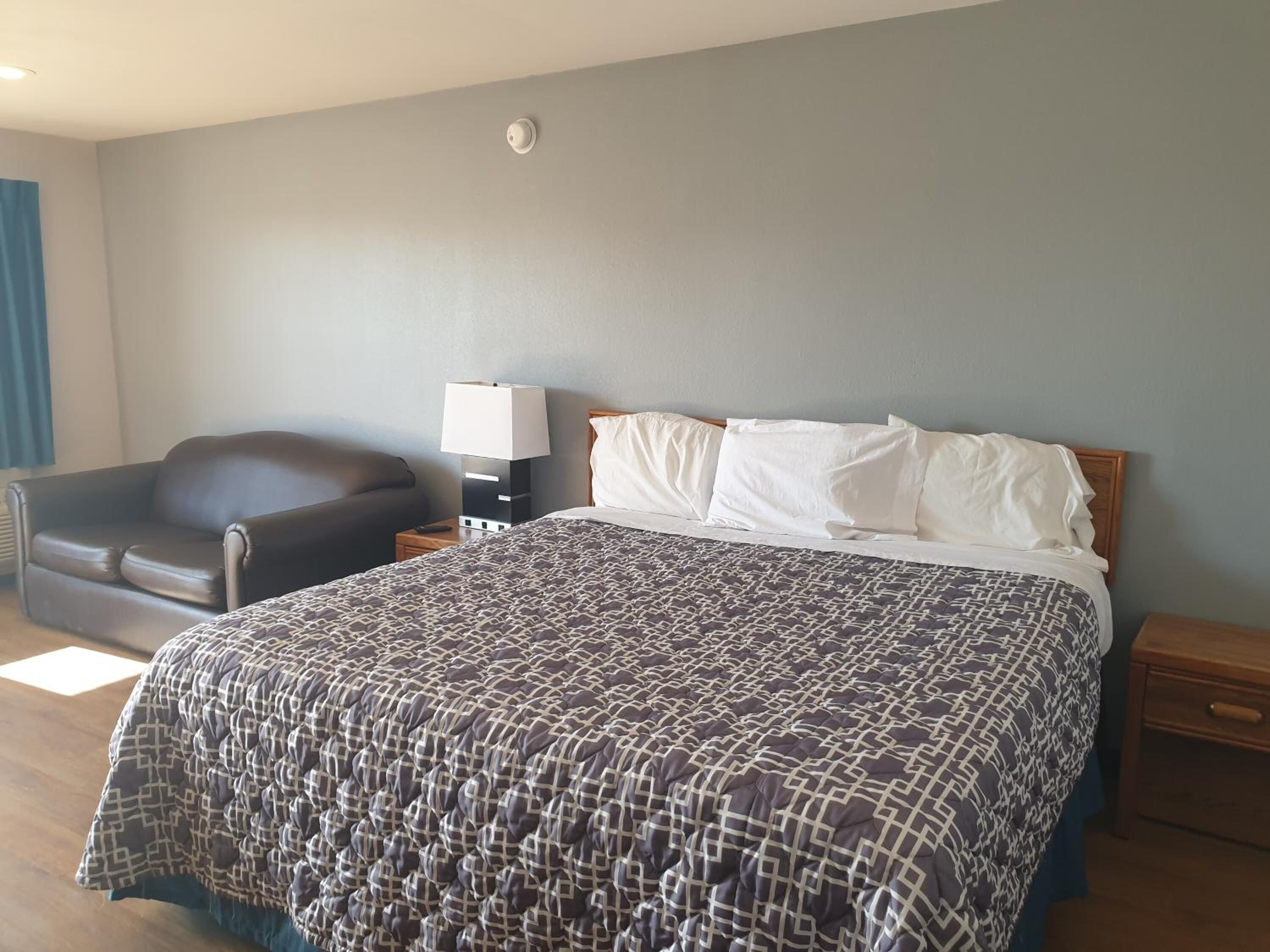 Una habitación de hotel con una cama, una silla, una mesita de noche y una lámpara.
