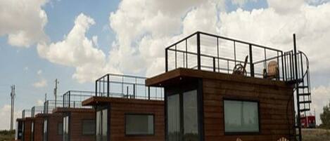 A row of wooden cabins with a glass front, a wooden deck, and a chair.
