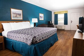 A hotel room with a large bed, a desk with a television, a chair, and two framed pictures on the wall.