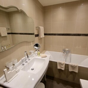 A bathroom with a sink, mirror, toiletries, and a bathtub. - Adriatica Hotel (Geneva)