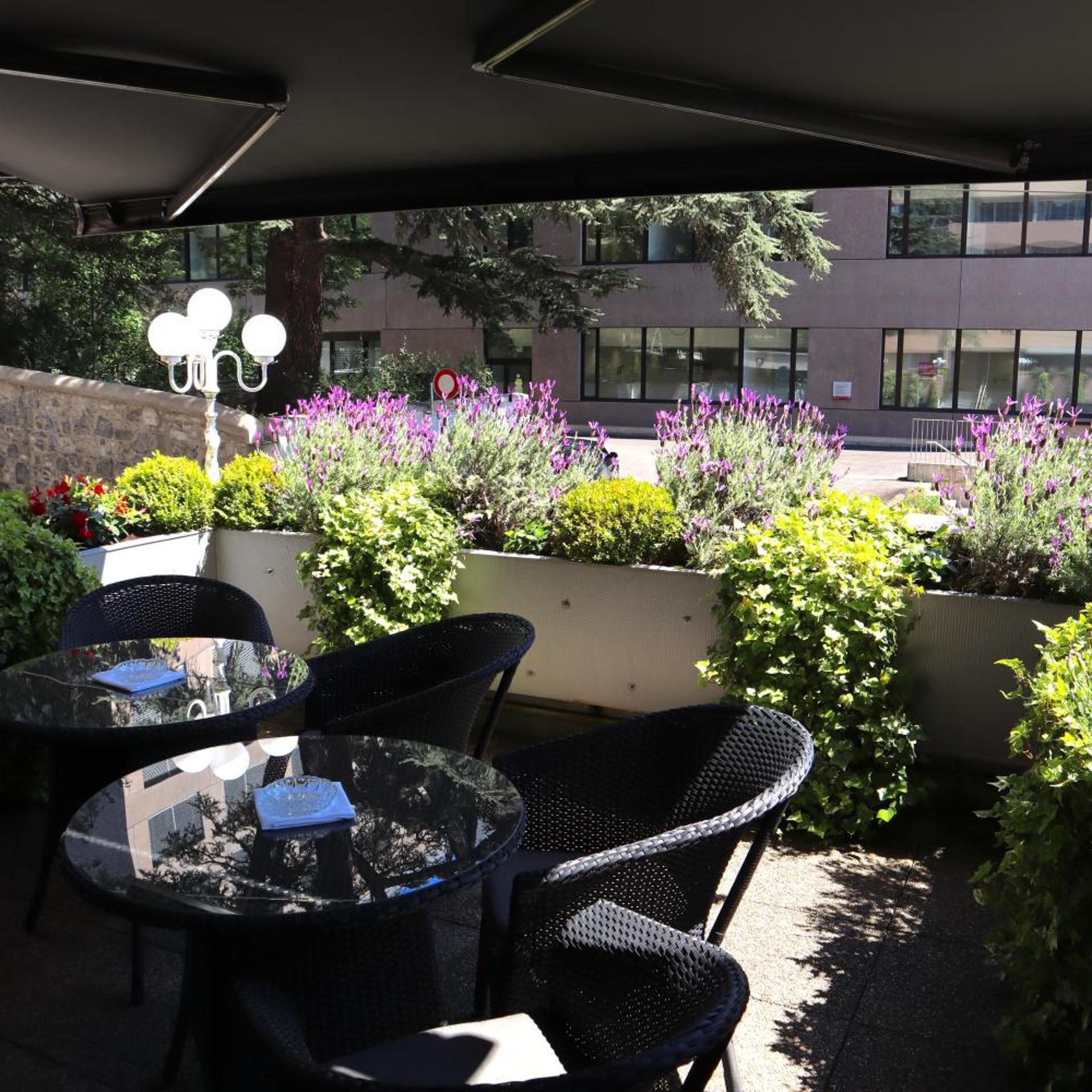 Uteservering med bord och stolar, omgiven av planterade växter och blommor.