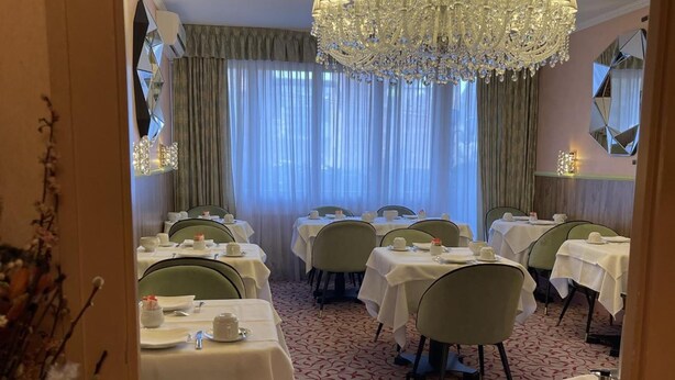 Un espace repas avec des tables dressées, un lustre et une moquette à motifs.