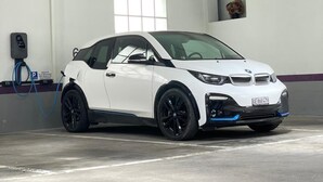 Un vehículo eléctrico blanco cargando en un estacionamiento subterráneo con pisos de concreto y paredes blancas.