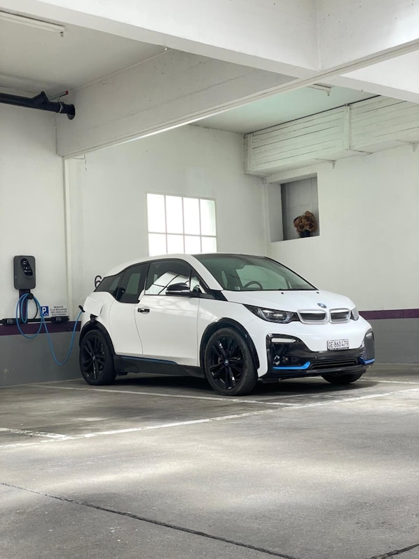 A white electric vehicle charging in a parking garage with concrete floors and white walls.