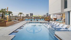 Une piscine sur le toit offrant une vue dégagée sur les gratte-ciel de la ville, entourée de chaises longues et d’un espace bar.