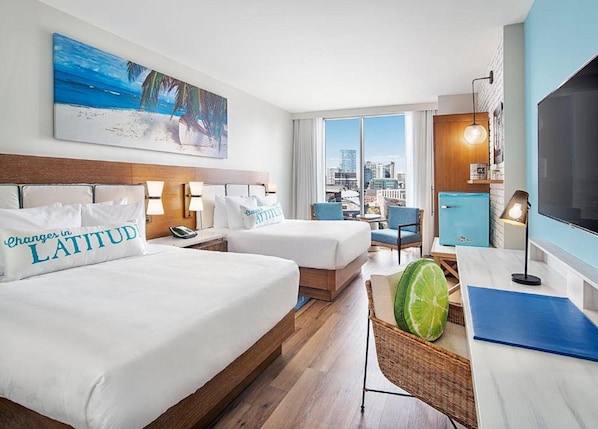 A hotel room with two beds, a city view, a painting of a beach, and a large TV.