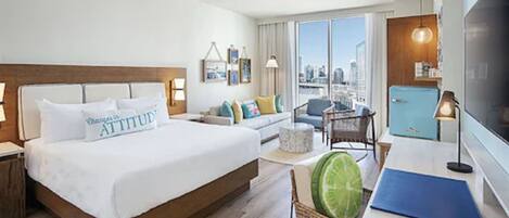 Ein Hotelzimmer mit einem großen Bett, einer Couch, einem Esstisch, einem Fernseher und Blick auf die Stadt.