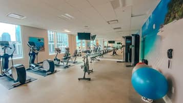 A gym with various exercise machines, a large blue exercise ball, and a mural on the wall.