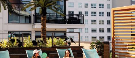 A poolside area with lounge chairs, a palm tree, and a building in the background.