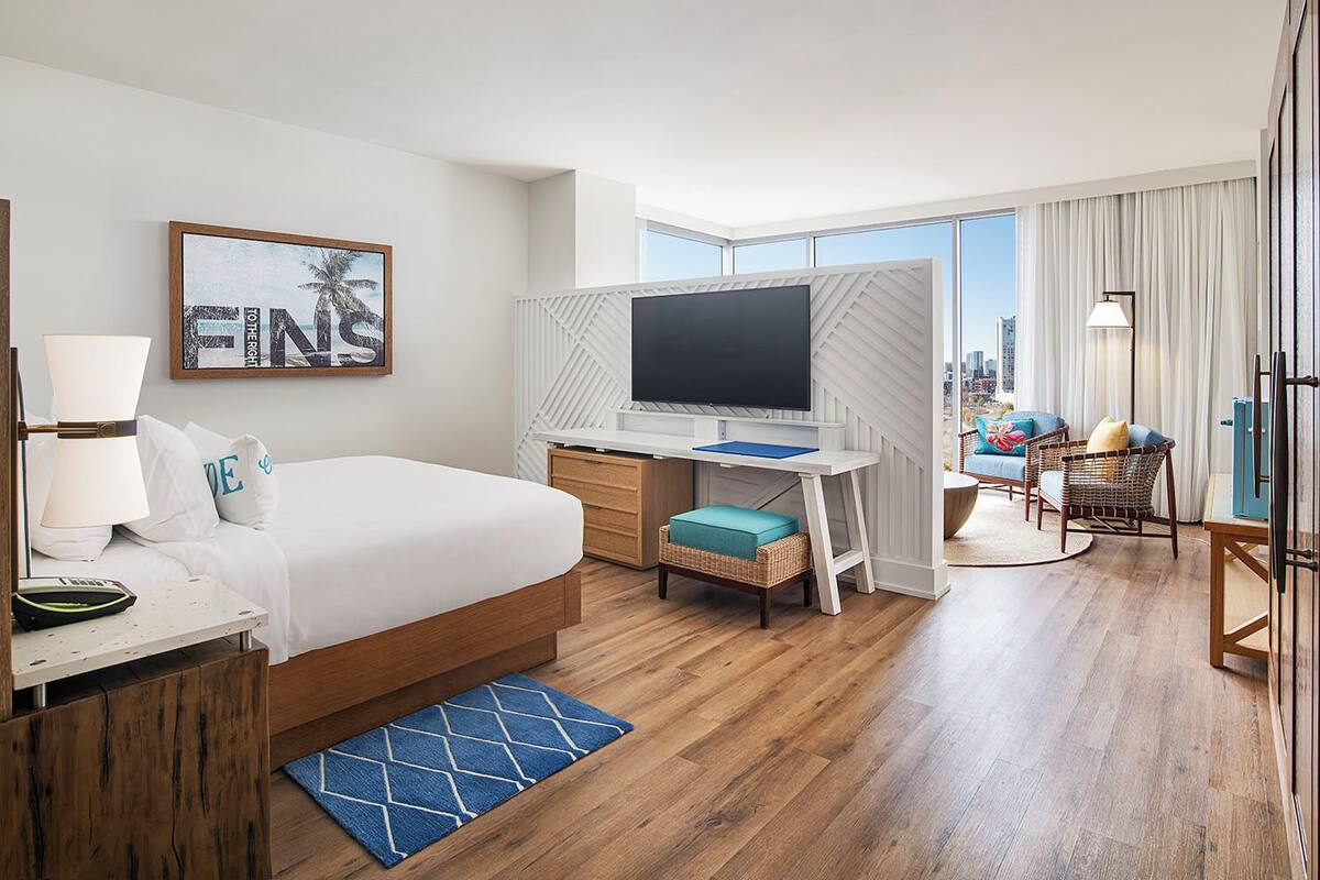 A hotel room with a bed, desk, TV, and a view of the city.