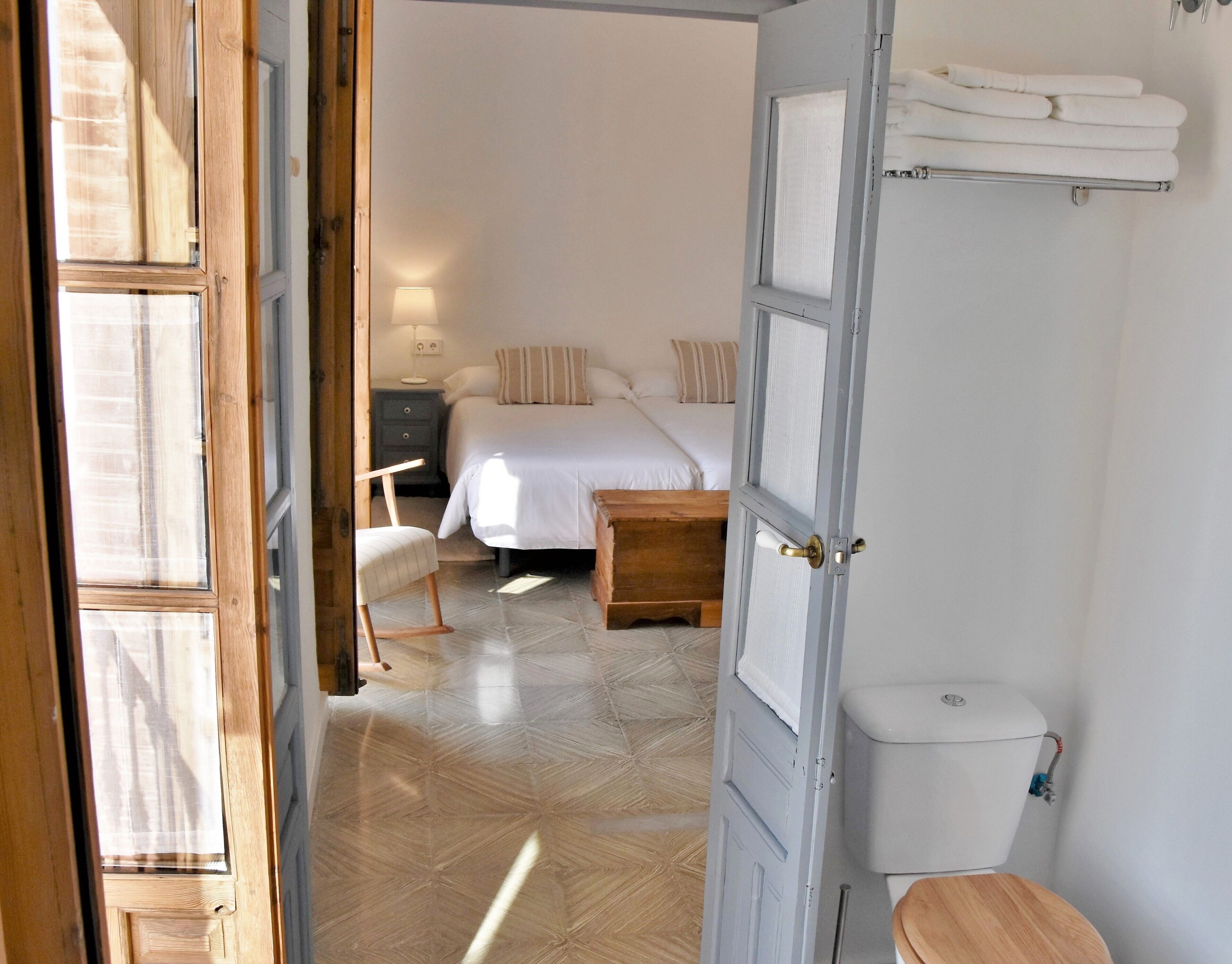 Een slaapkamer met een bed, nachtkastje, stoel en toilet.