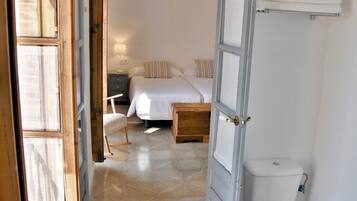 Een slaapkamer met een bed, nachtkastje, stoel en toilet.