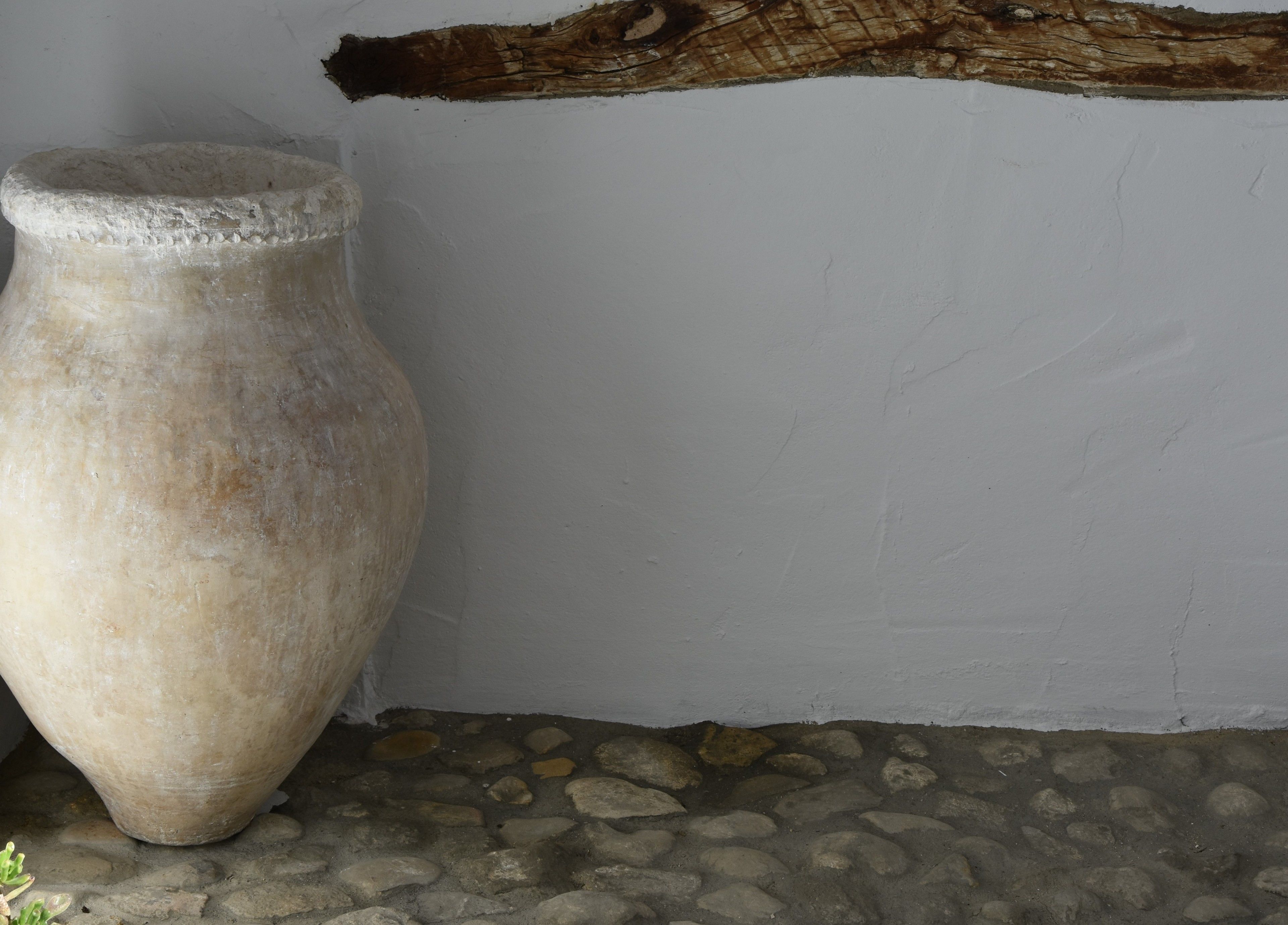 A large, weathered stone vase against a plain wall and stone floor.