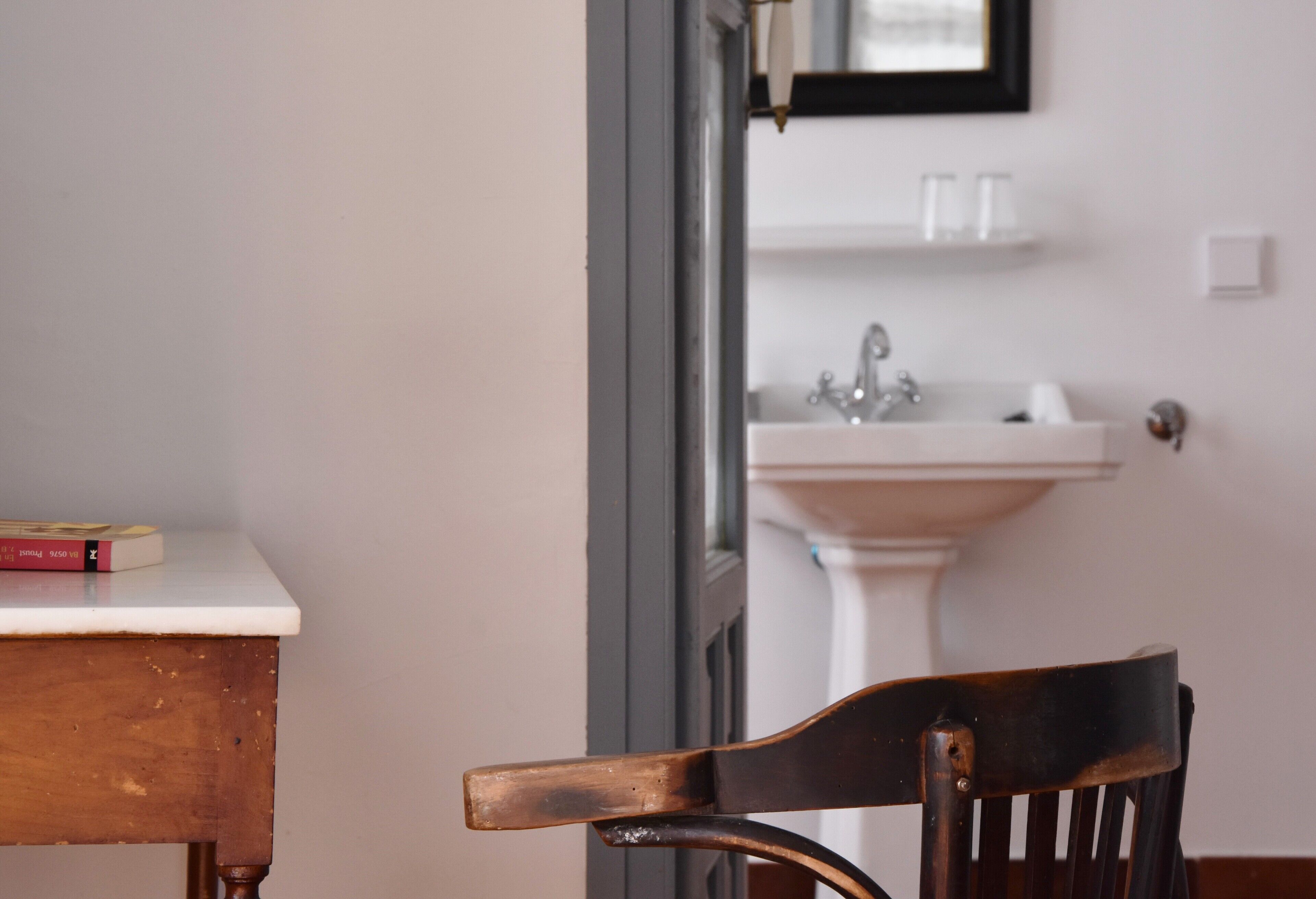 Una silla de madera en una habitación con una mesa y un lavamanos blancos al fondo.