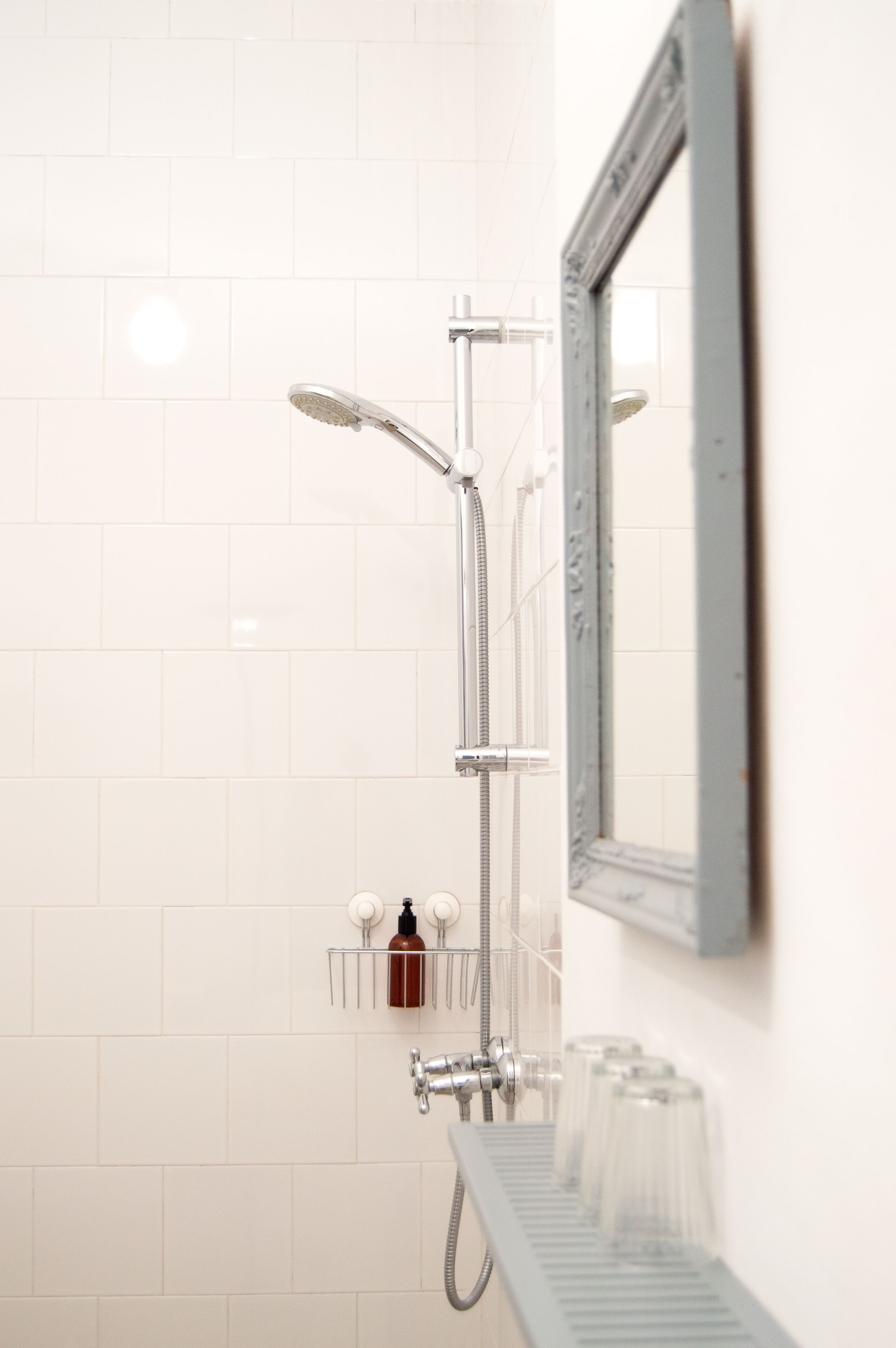 Een badkamer met een douche, een spiegel en een zeepdispenser op een plank.