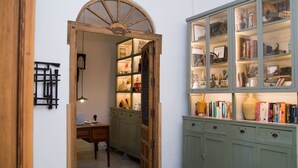 Un pasillo con una puerta de madera que da a una habitación, un armario verde con puertas de cristal y un escritorio con una lámpara.