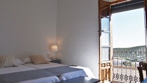 Un dormitorio con dos camas, una mesita de noche con lámpara y un balcón con vistas al paisaje.