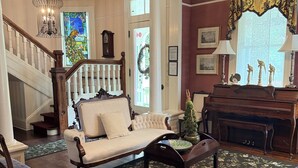 A traditional living room with a sofa, chairs, a piano, and a staircase. - Peacock Place (Eastman)