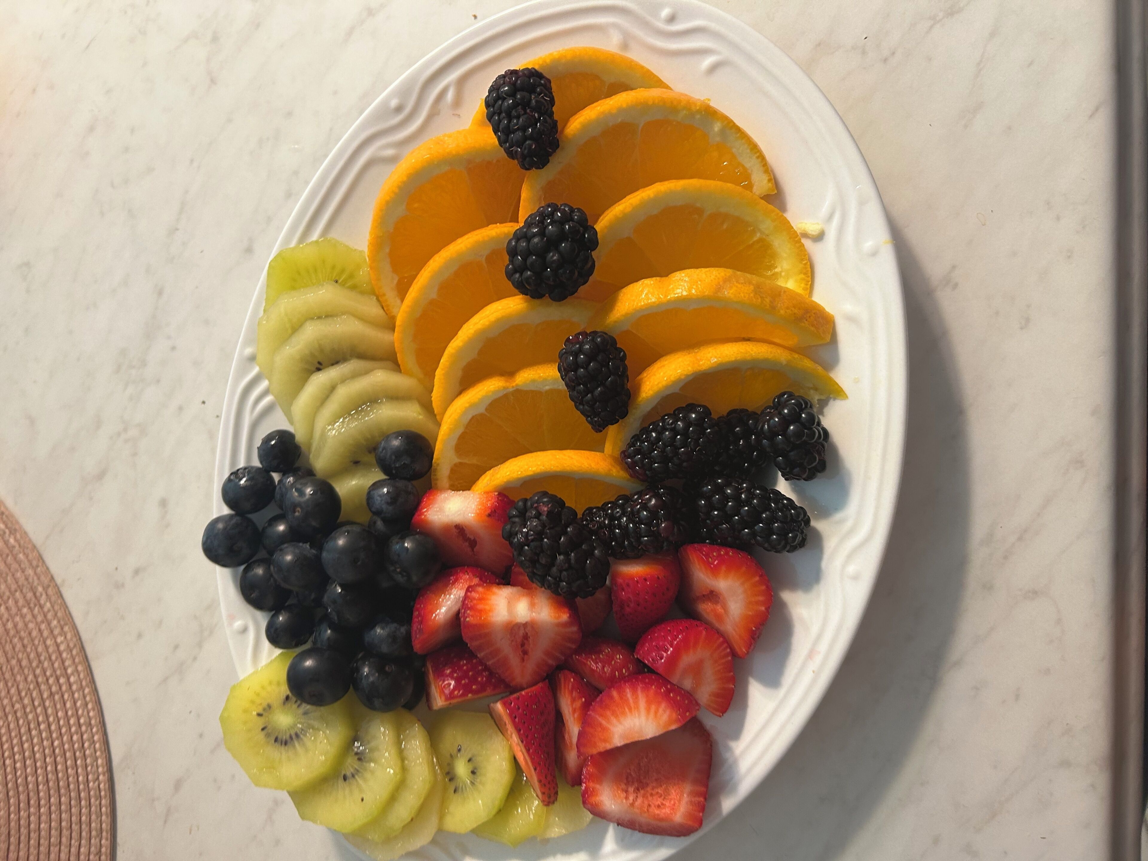 Un plato blanco con frutas cortadas, incluyendo kiwi, fresas, arándanos, frambuesas y gajos de naranja.