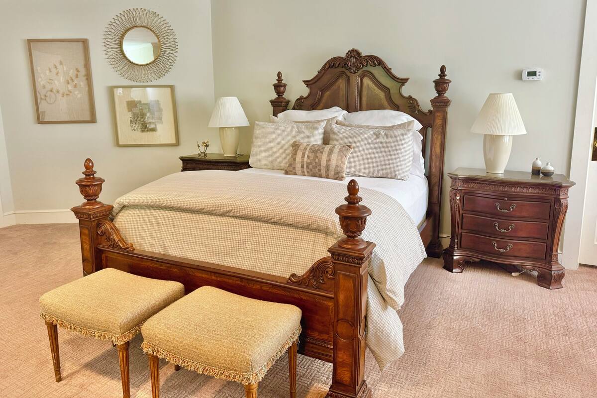 Quarto arrumado com cama de madeira, duas mesas de cabeceira, um criado-mudo e um espelho na parede.