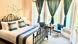 A bedroom with a large bed, two chairs, a table, and a window with curtains. - Peacock Place (Eastman)