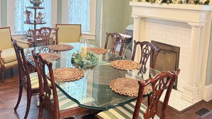 A dining room with a glass table surrounded by wooden chairs, a chandelier, and a fireplace with decorative plates above. - Peacock Place (Eastman)